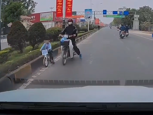 Người đàn ông đi xe máy kèm bé trai tập xe đạp đi ngược chiều